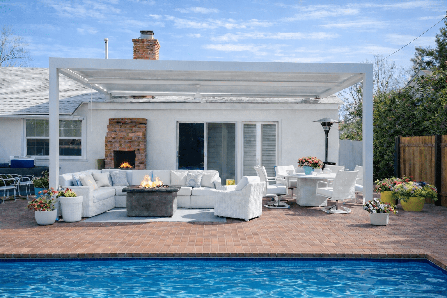 Modern white outdoor patio set by a pool with a fire pit and dining area.