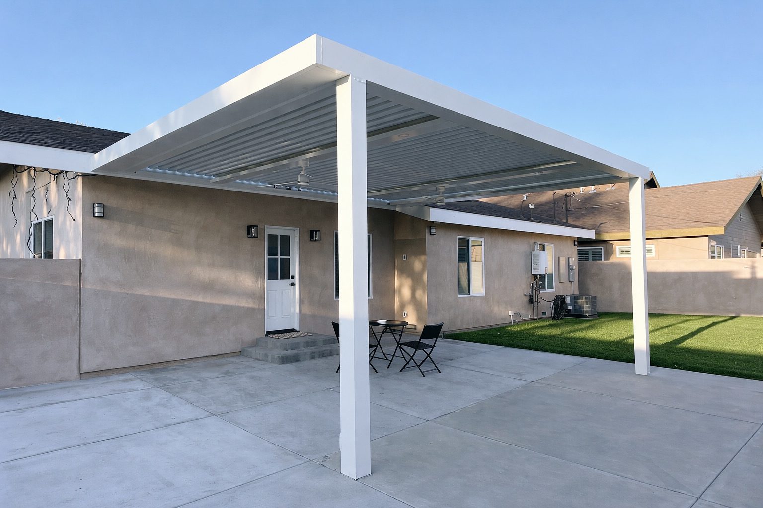 Modern patio cover with adjustable slats over concrete and lawn area.