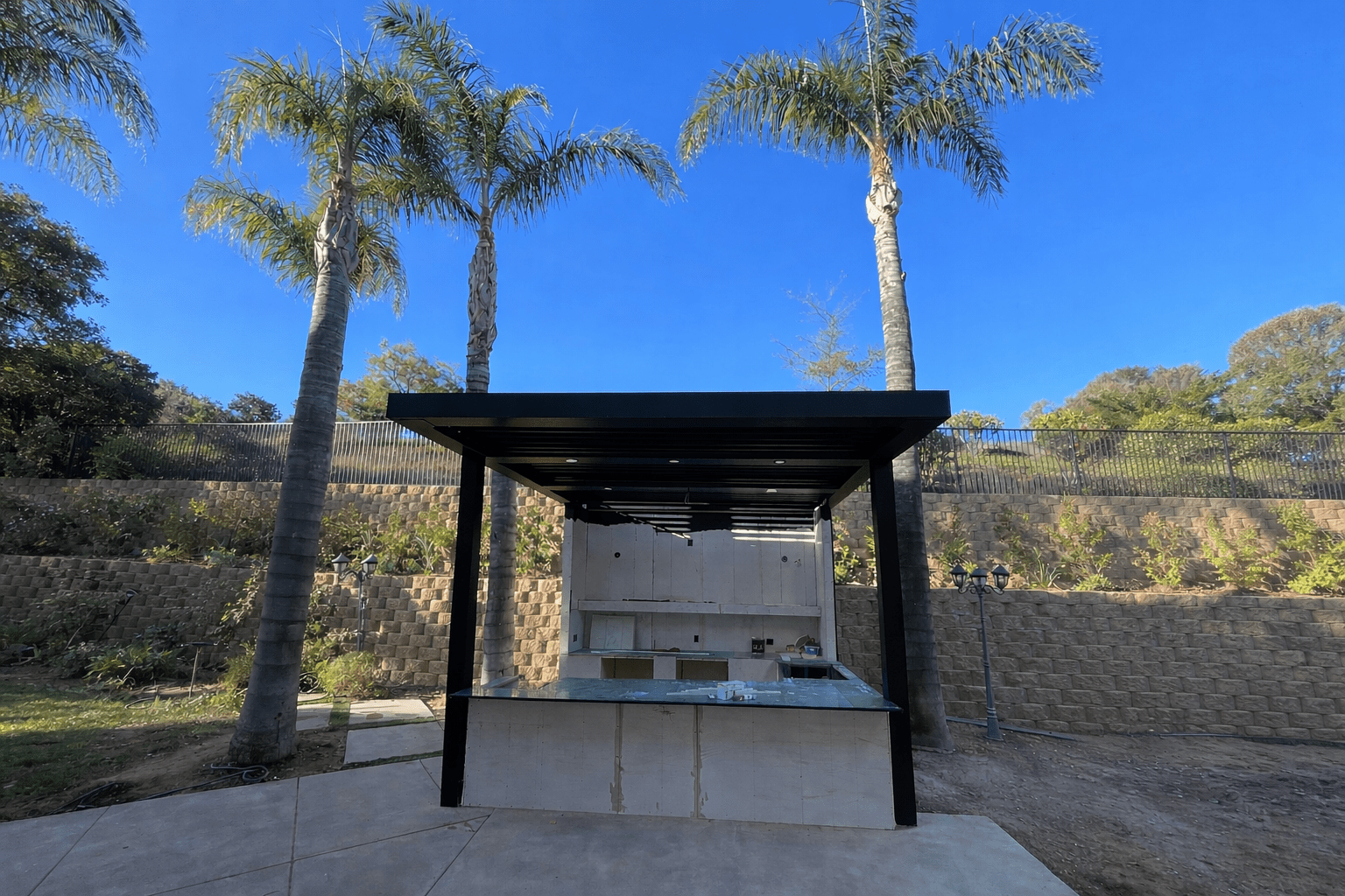 Outdoor grilling station with palm trees and clear sky.