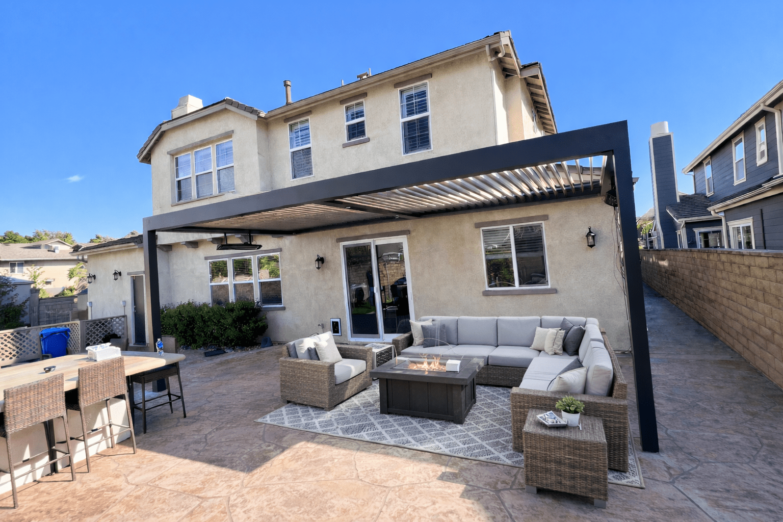 Cozy outdoor patio with comfortable seating and a modern pergola attached to a two-story house.
