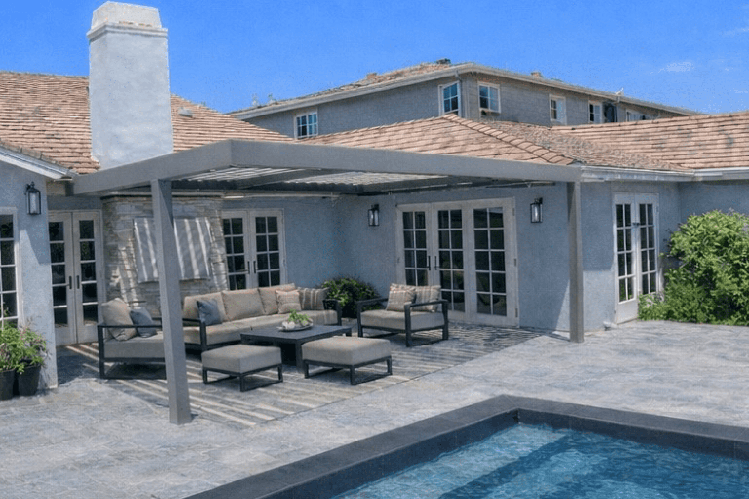 Cozy backyard patio with seating and pool under a pergola.